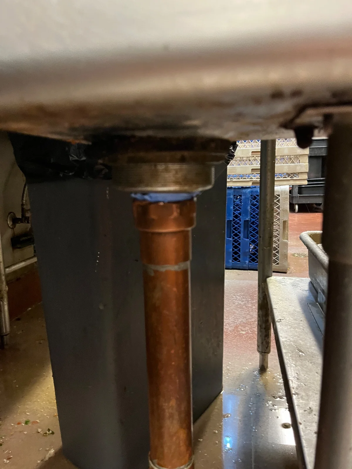 Copper drain pipe attached below a stainless-steel sink strainer.